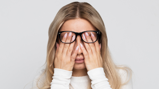 femme blonde avec des lunettes qui cachent son visage dans ses mains car elle est fatiguée