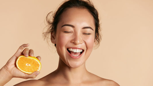 femme avec une orange dans la main qui sourit sur un fond beige